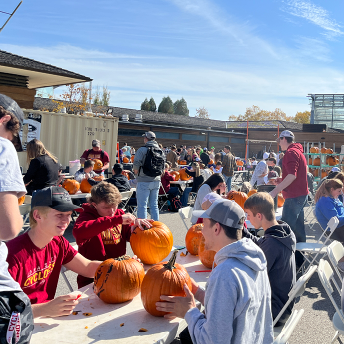 A hoard of volunteers work on pumpkin carving outside on a beautiful fall day.
