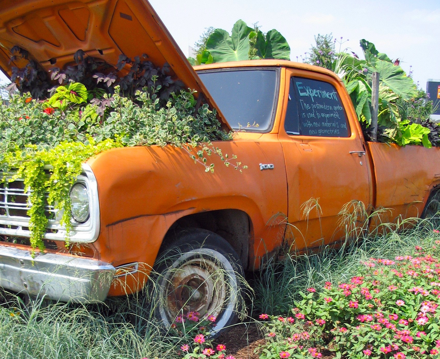 an orange truck in a garden surrounded by flowers, planted under the hood with various plants