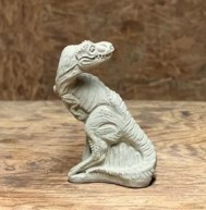 a small concreate sculpture of a dinosaur (maybe a raptor) with its head twisted to look behind it