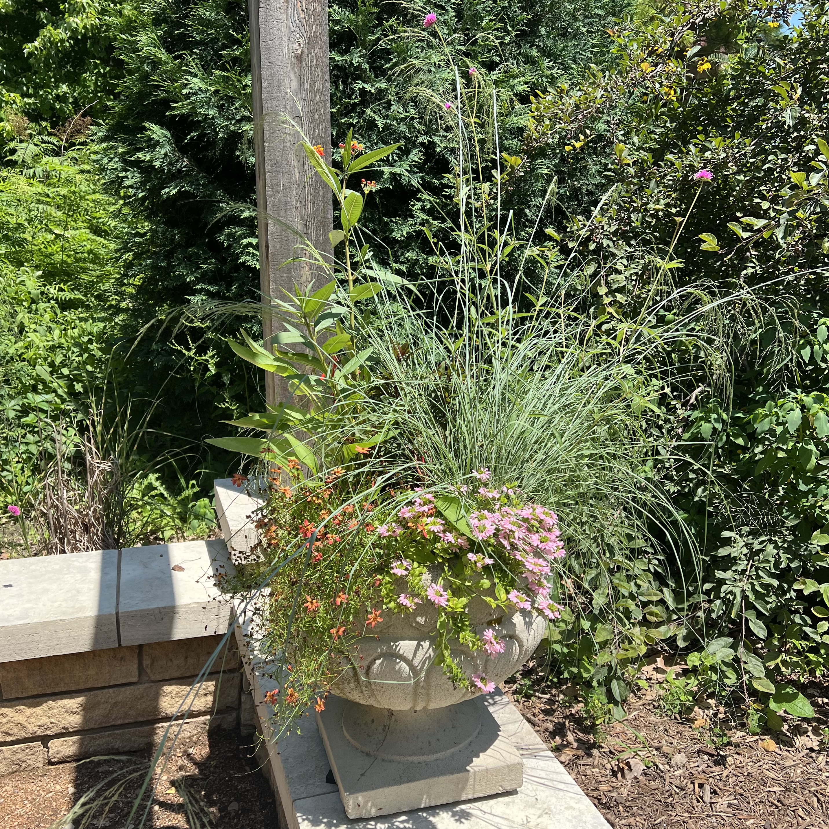A stone container with a mix of annual flowers and prairie grass