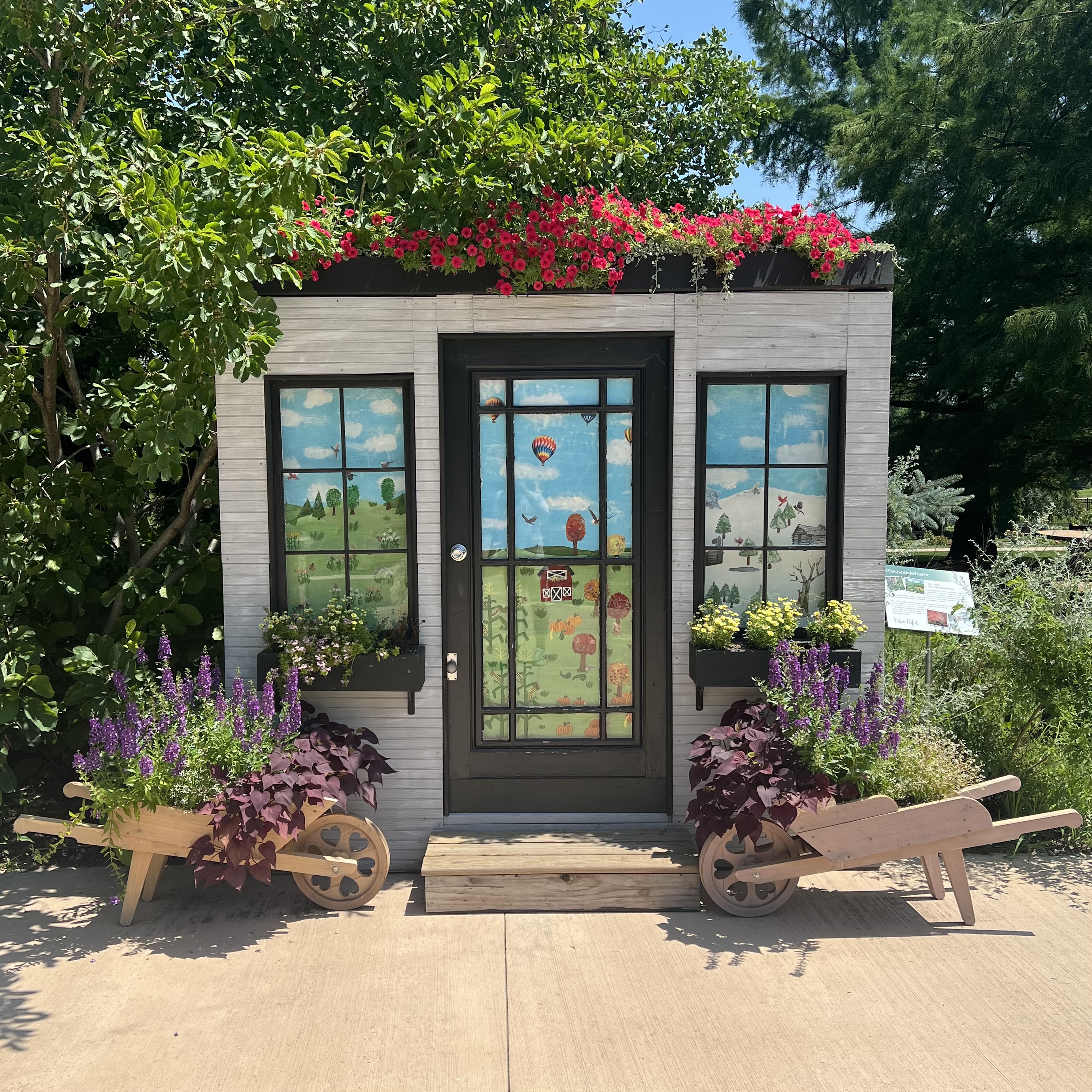 A window display with flowers in planter boxes and wheelbarrows