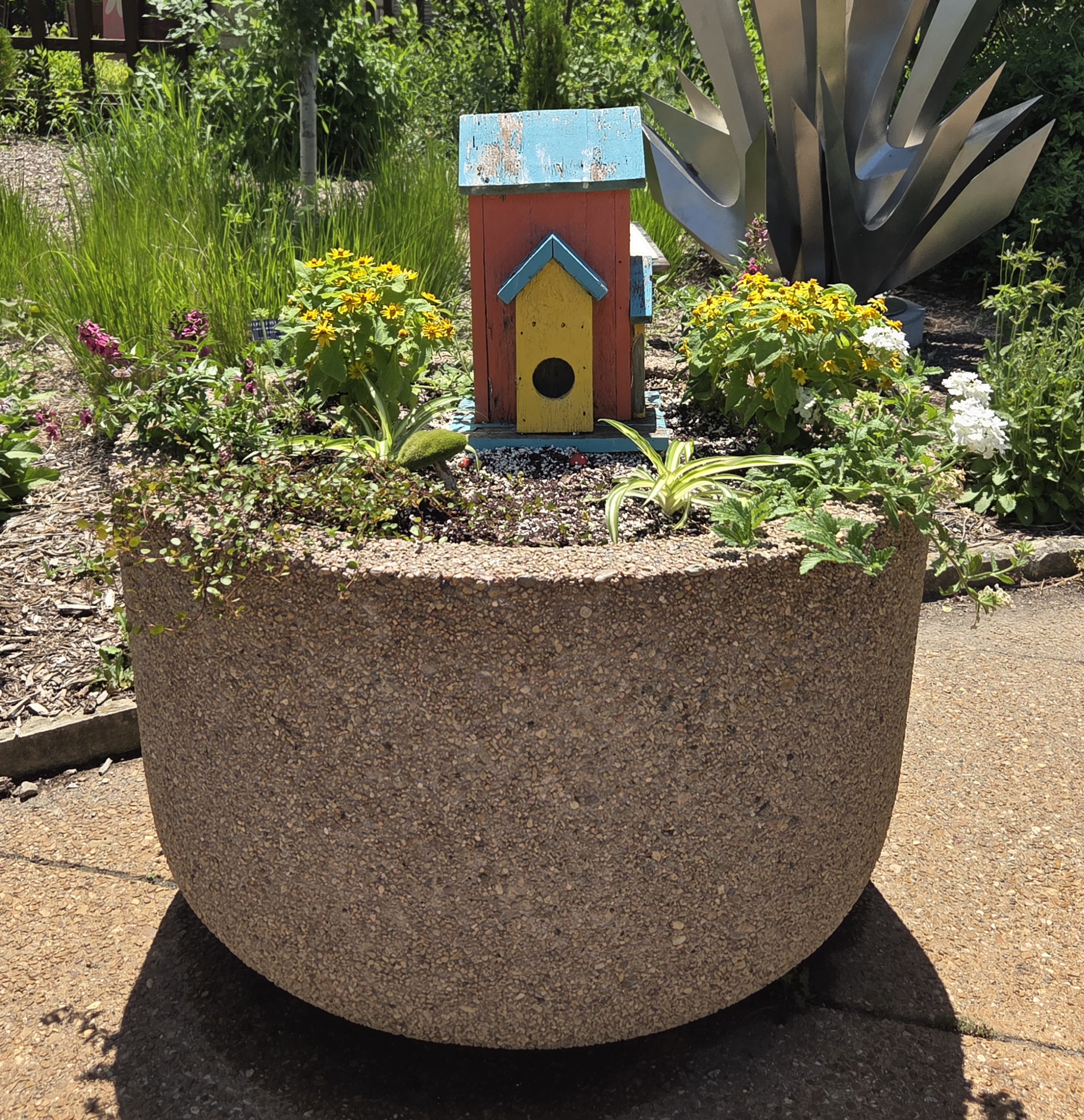 A container with a red birdfeeder and multiple plants