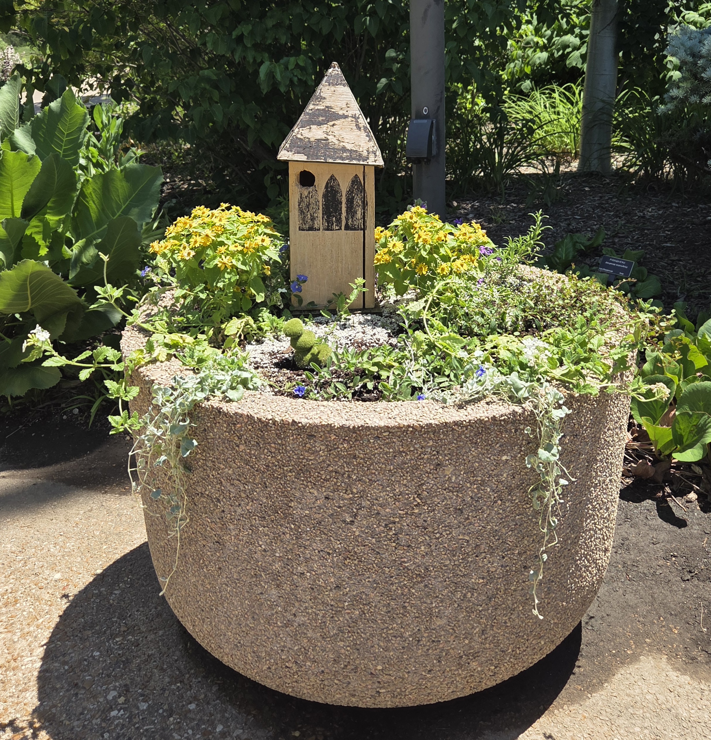 A container with a white birdfeeder and multiple plants