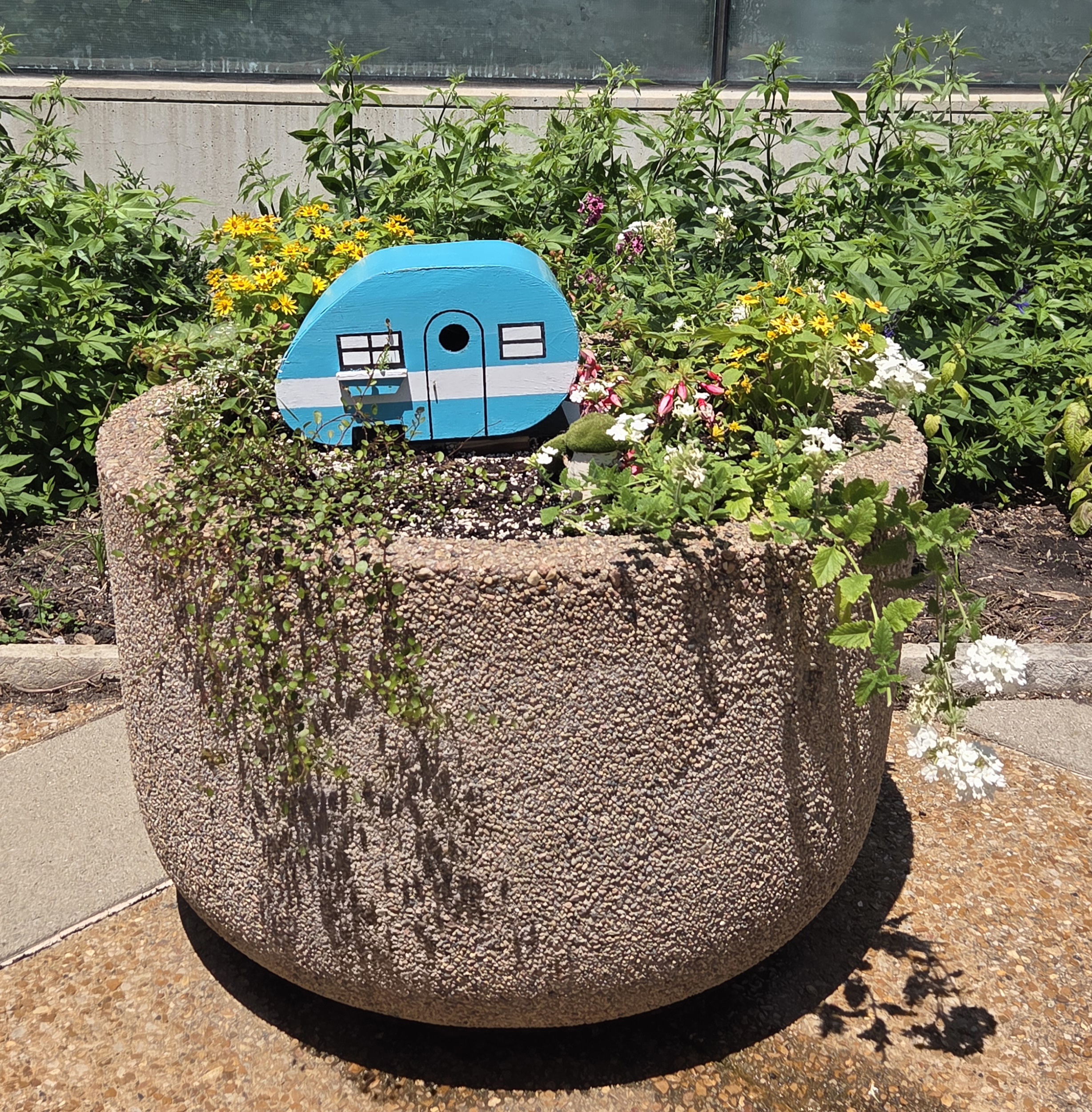 A container with a blue bird feeder and multiple plants 
