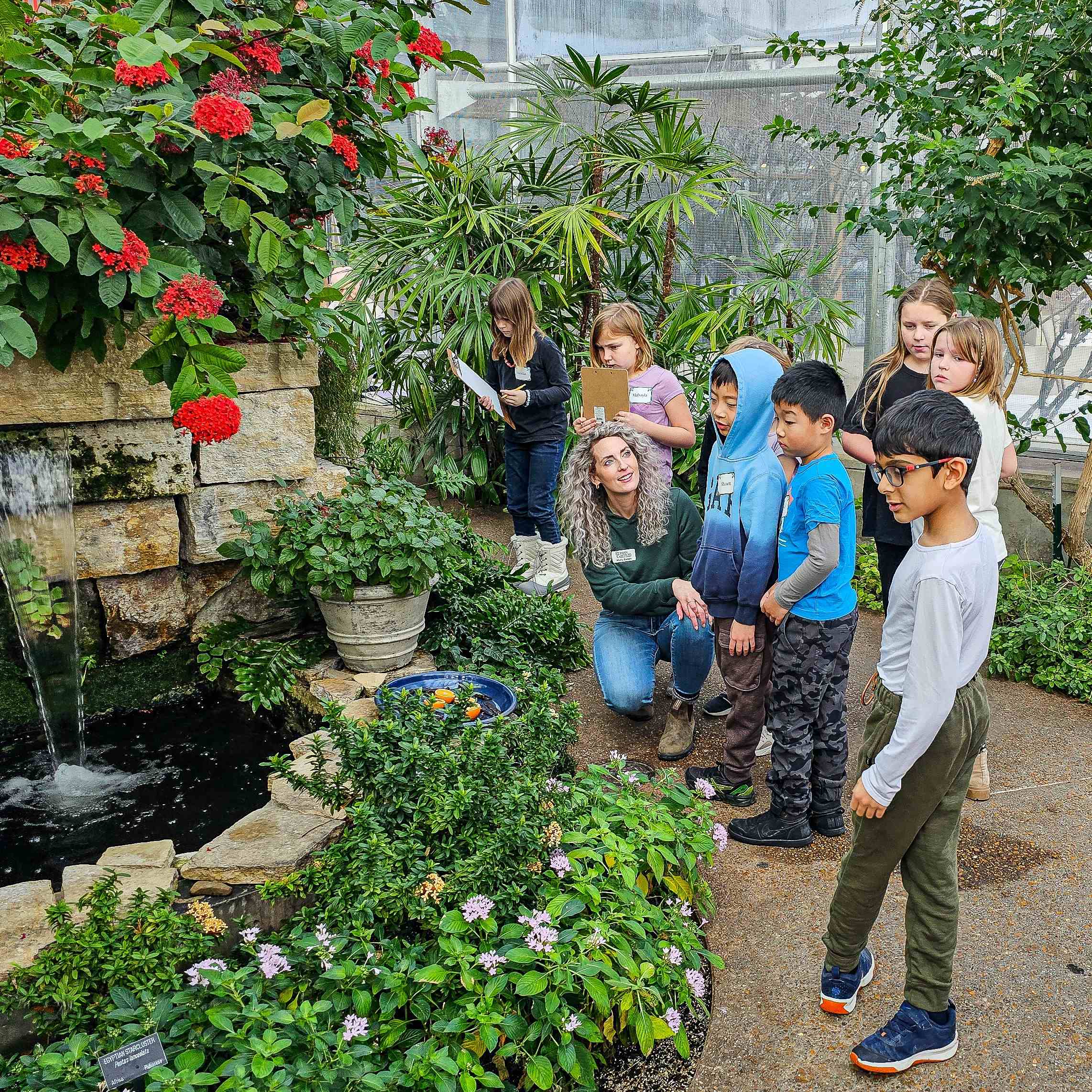 Teacher kneels next to a group of children in an indoor garden