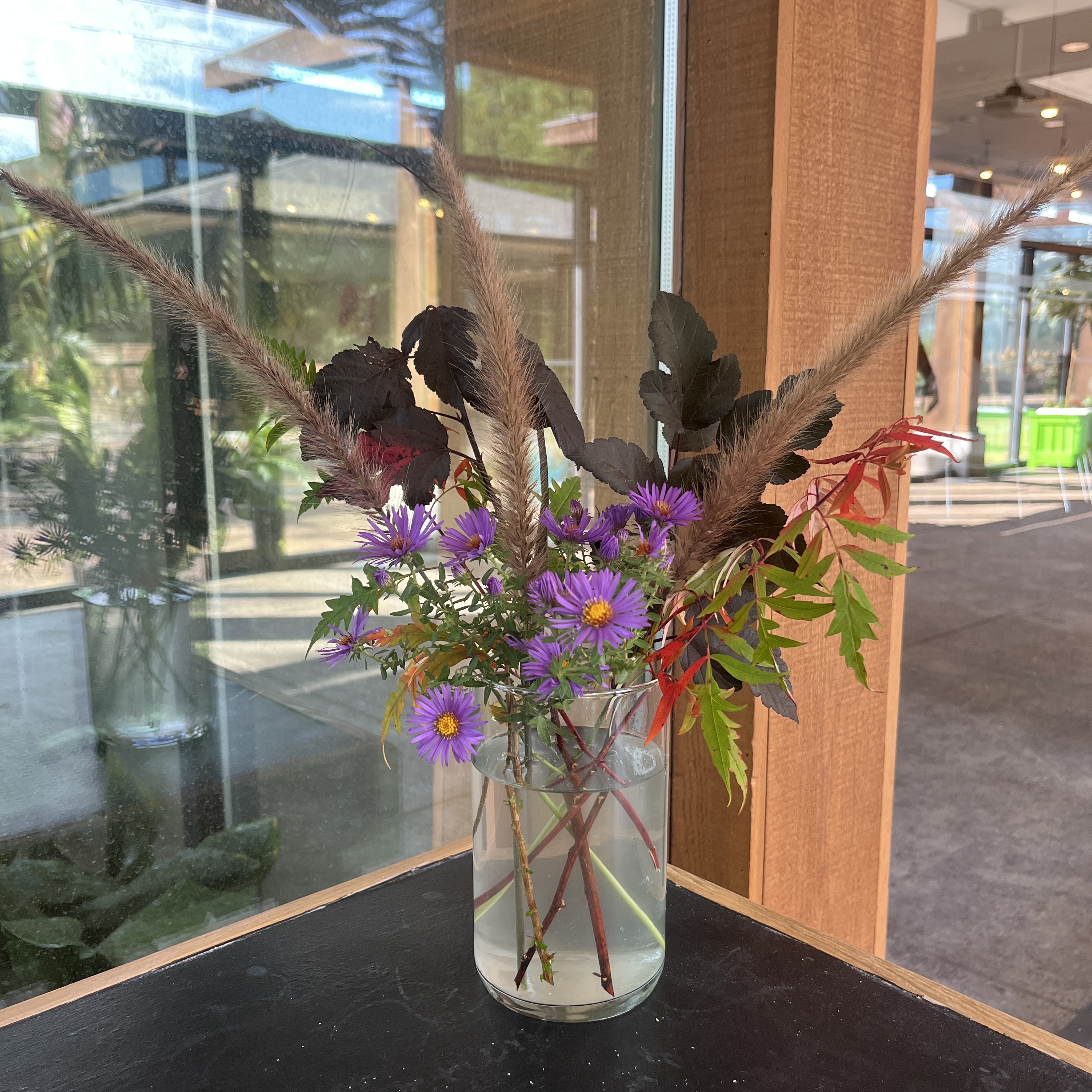 Bouquet with bright purple flowers, textured grass, and fall foliage branches.