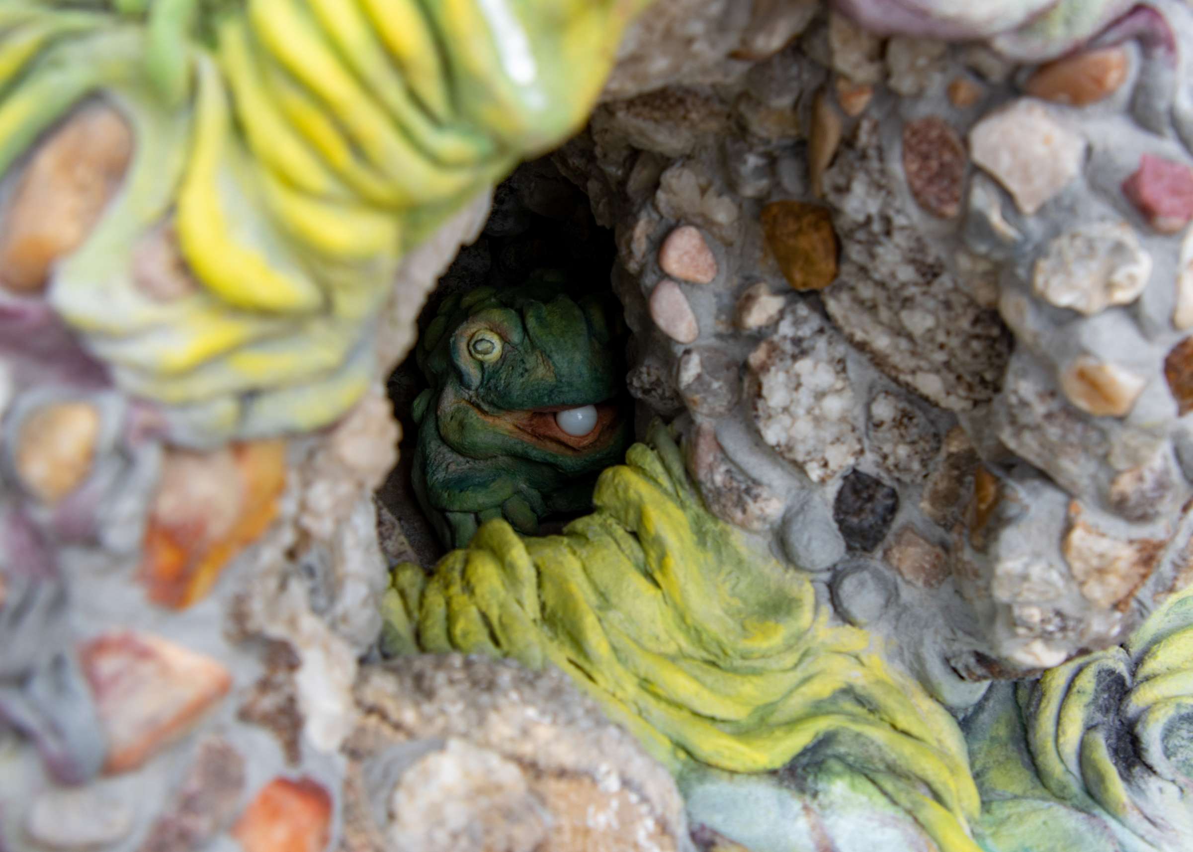 A frog in a hole holds a pearl in its mouth. This is a piece of artwork for Spring Enchantment fairy houses.