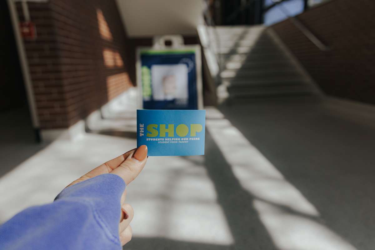a student's hand holds The SHOP's business card in the halls of Beyer Hall at Iowa State University.