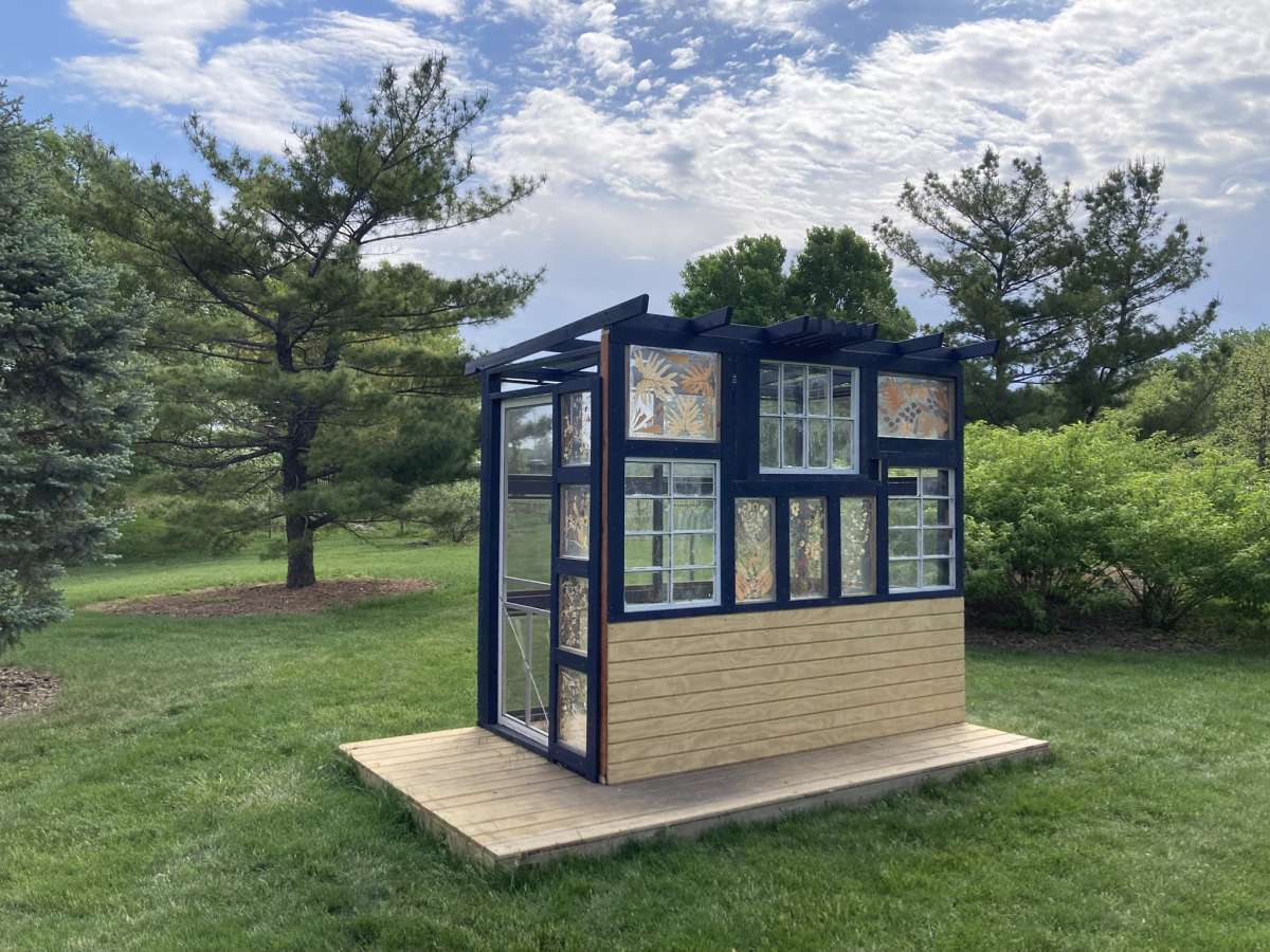 a modern greenhouse structure in a garden setting, with pressed flower windows and black painted framing