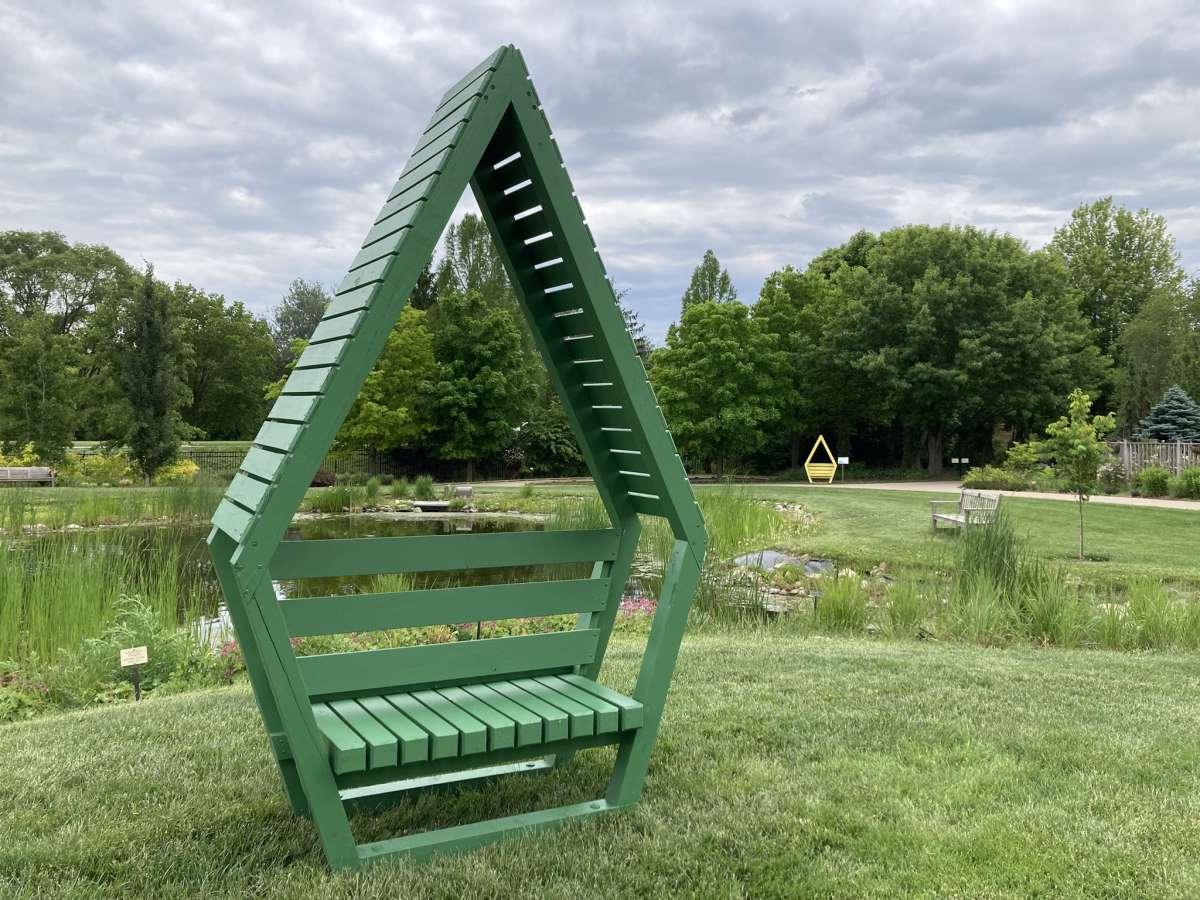 a diamond-shaped green chair in the foreground in front of a lake; a yellow diamond-shaped chair in the background