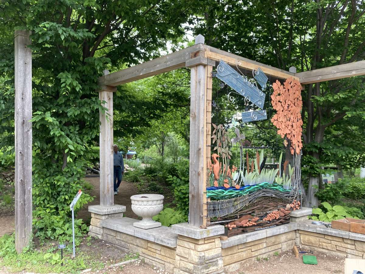 an installation in a garden space of a wall made with metal, clay, and other found objects creating a nature landscape