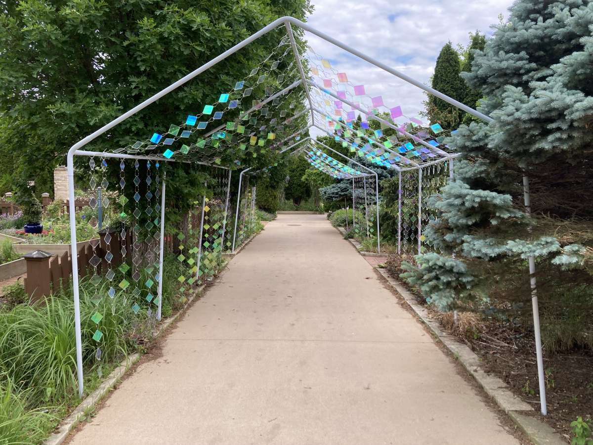 colorful reflective squares draped over the tops and sides of a pathway in a garden