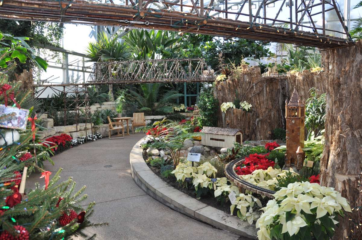 a partial view of an indoor plant conservatory decorated with a garden-scale railroad and replica Iowa State University buildings