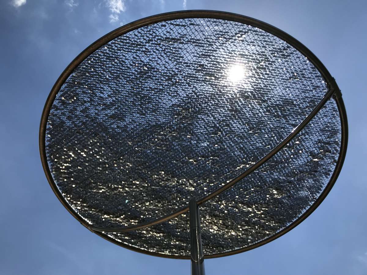 a view of the top of a circular, metal kinetic sculpture that reflects the sunlight and clouds in the surrounding sky