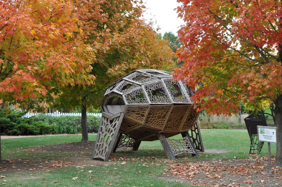 a fall scene in a garden with a seed-pod shaped treehouse on three legs between two trees
