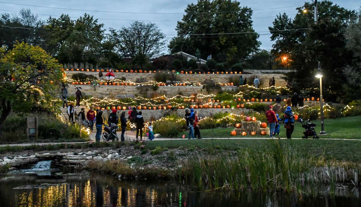 Adults and children viewing lighted pumpkins on a hillside garden