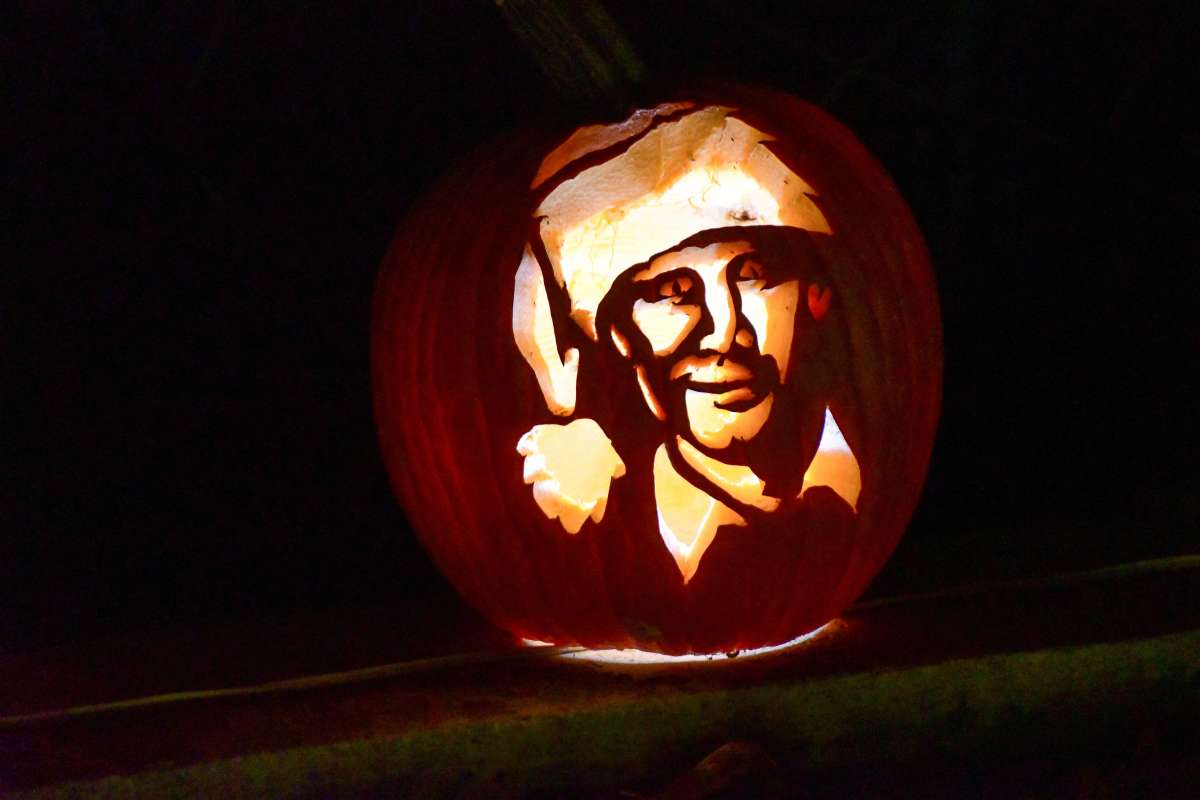 A pumpkin carved with a detailed face wearing a Santa hat illuminated from inside against a dark background.