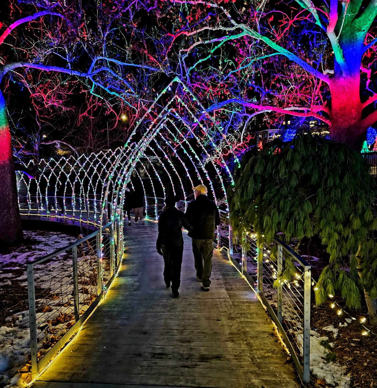 Two people walking through a lighted tunnel of gothic arches.