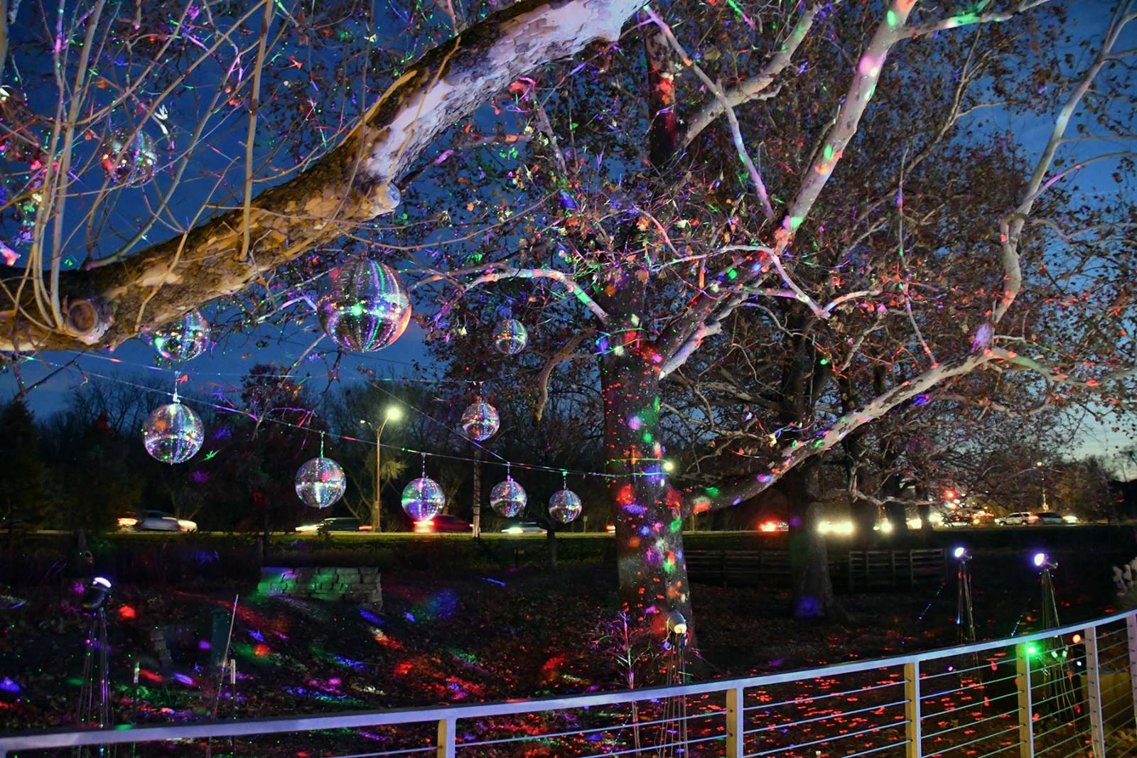 Sparkling disco balls hang and reflect lights which sparkle against all of the trees, landscape, and bridge.