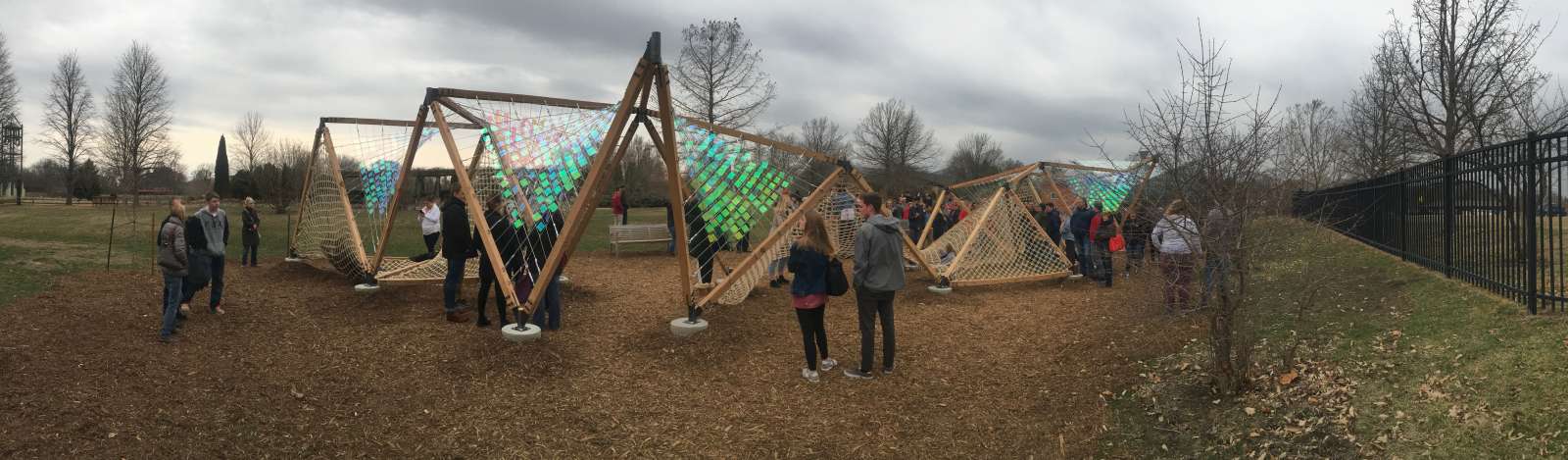 a panoramic view of an interactive art installation with reflective iridescent squares and marine netting surrounded by people