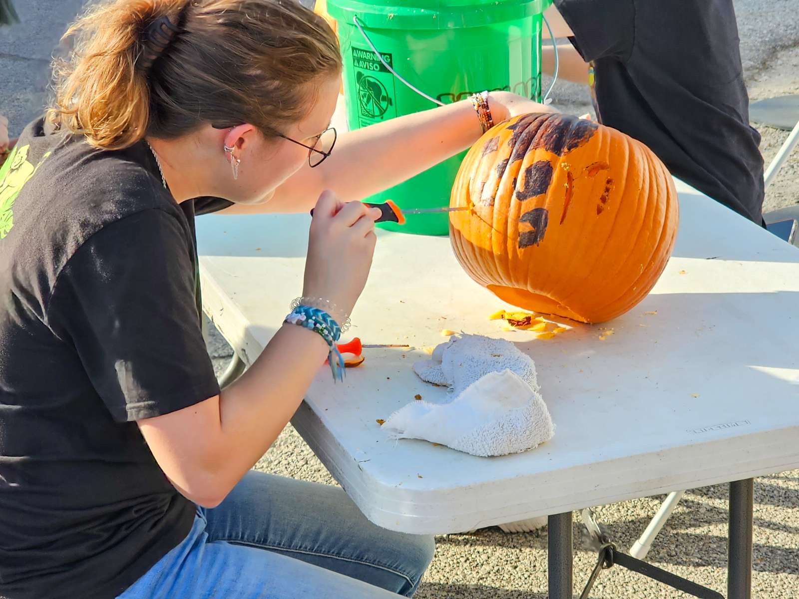A volunteer carefully carves a design already drawn onto a pumpkin.