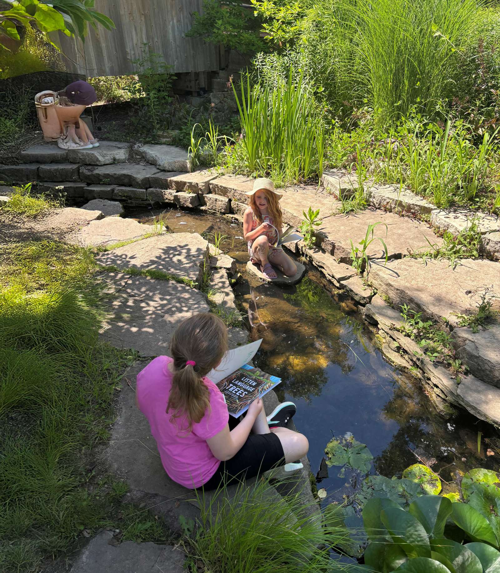 Girls reading books by a stream in a garden