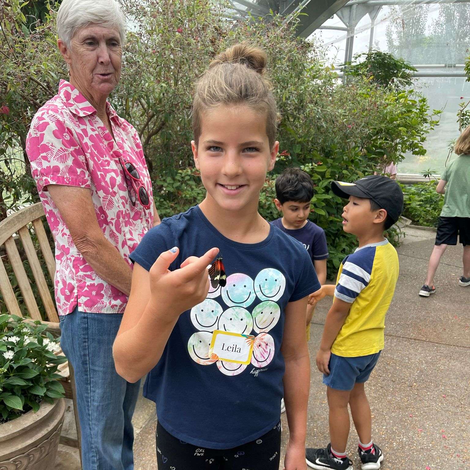Girl with a butterfly perched on her finger in a tropical indoor garden