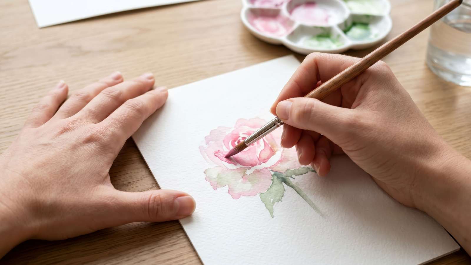 Person painting a watercolor painting of a rose