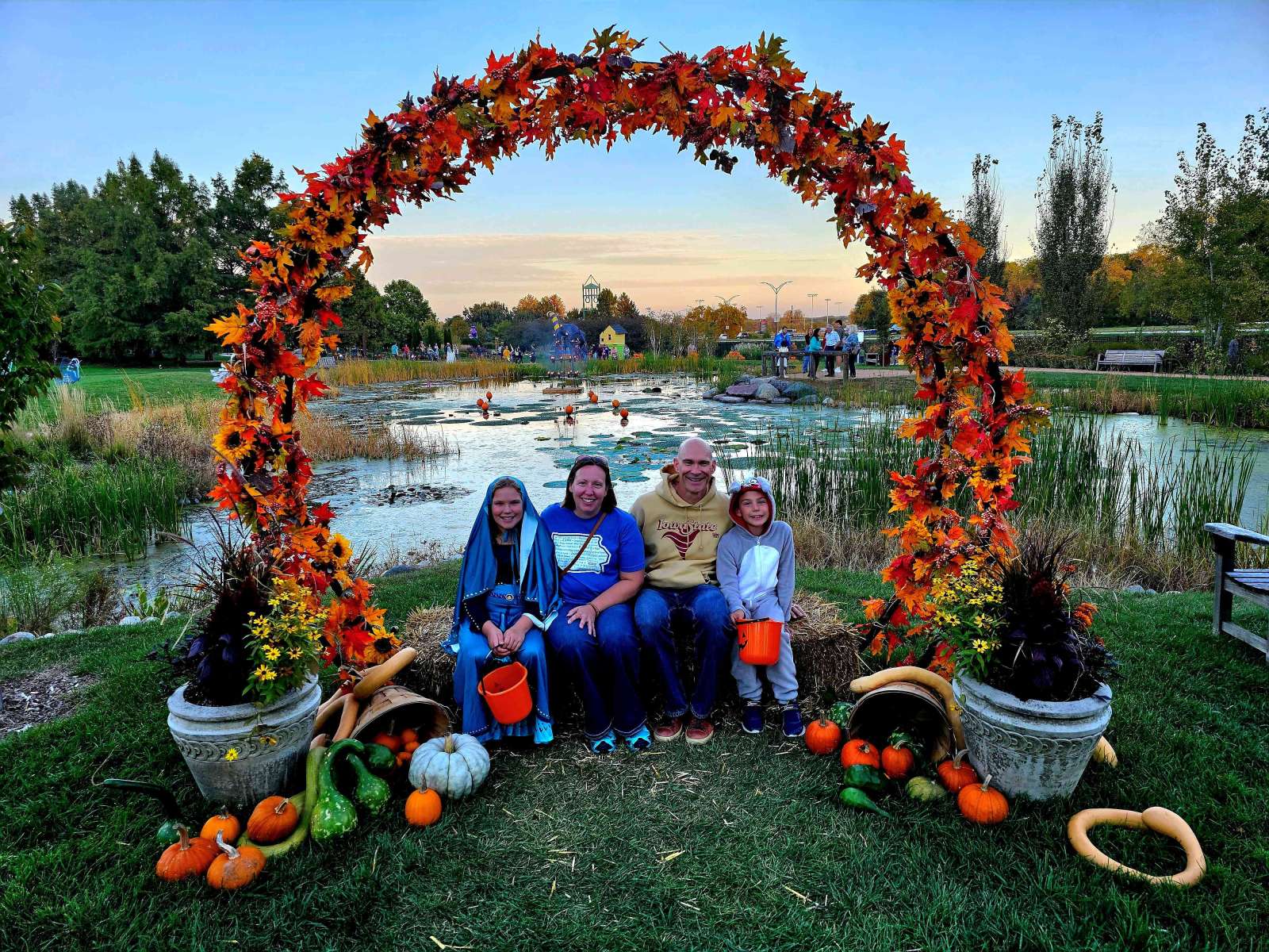 People posing in costume under a leaf covered arch in front of a lake