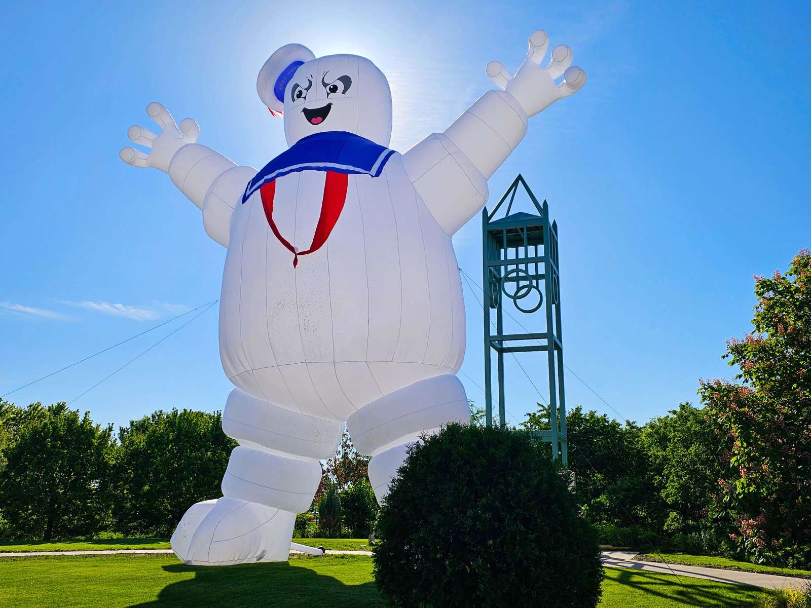 Giant Stay Puft Marshmallow man inflatable in a garden setting with a campanile.